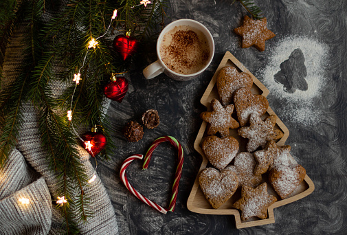 Gingerbread with cocoa and sweets on a gray background with spruce branches, Christmas decorations and a gray knitted blanket. Flatlay.