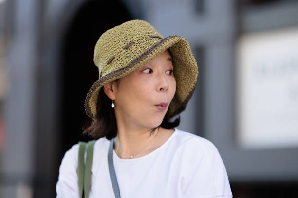 Asian woman outdoors wearing a hat with a surprised expression