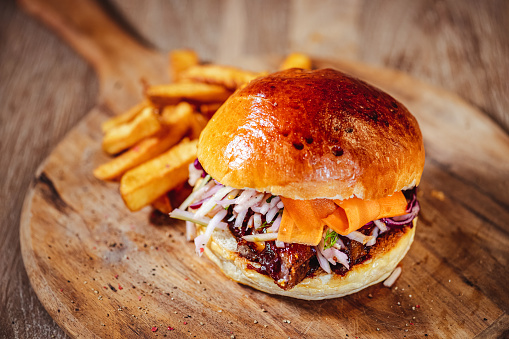 tasty burger with pork ribs, carrots, onion dipped with spicy sauce on a wooden cutting board