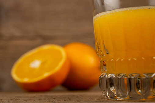 Glass of orange juice with half oranges on vintage table