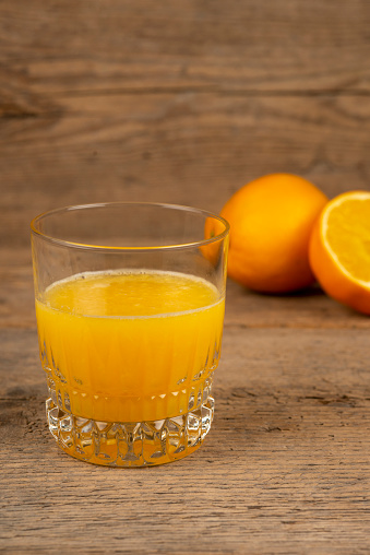 Glass of orange juice with half oranges on vintage table