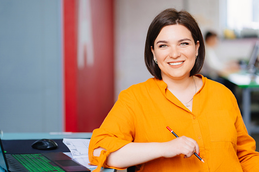 a woman wearing a orange blouse with laptop in a office. the concept of a business female portrait. office rent for an hour.