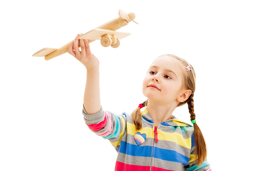 Beatiful smiley girl playing with old-fashioned wooden toy plane isolated on a white background