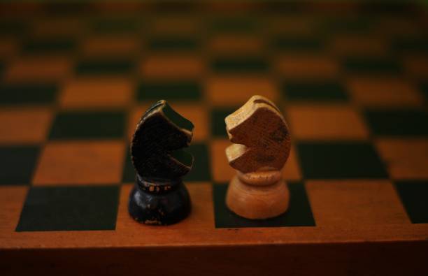 Two horse pieces on a chessboard, one black and the other yellow facing each other