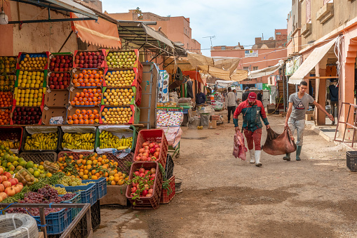 Market palce in Morocco. Two men lug a load past market stalls including fruits and vegetables