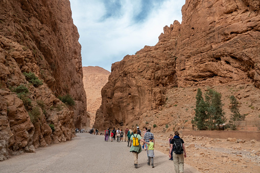 People are walking in the dramatic scenery of the Todra Gorge (called locally Toudgha Gorge), a natural oasis in the desert created by the River Todra carving its way through limestone for many centuries. Walls reach over 400 metres in height