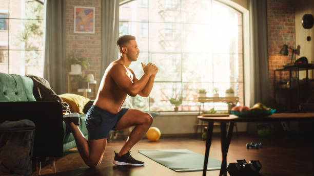Strong Athletic Black Man Does Shirtless Workout at Home, Single Leg Squatting. Fit Muscular Sportsman Staying Healthy, Training Mind, Body. Sweat and Determination. Side View Wide Angle Camera Shot el hombre negro atlético fuerte hace entrenamiento sin camisa en casa, en cuclillas de una sola pierna. deportista musculoso en forma manteniéndose saludable, entrenando la mente, el cuerpo. sudor y determinación. vista lateral gran angular cámara shot