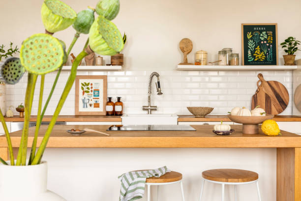 istock Creative composition of kitchen interior with mock up poster frame, wooden kitchen island, simple barstool, vase with green flowers, silver tap and personal accessories. Home decor. Template. 1462192483