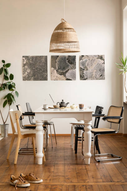 istock Warm dining room interior with mock up poster frame, elegant white table, rattan chair, shoes, cup, gray pitcher, wooden floor, plant, white wall and personal accessories. Home decor. Template. 1462192534