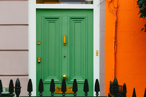 The colorful orange facade with green front door of a traditional terraced London mews townhouse.