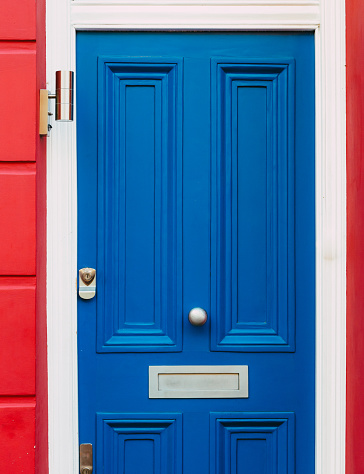 The colorful blue front door of a red traditional terraced London mews townhouse.