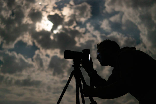 Man shooting the night cloudy sky under moon with a tripod