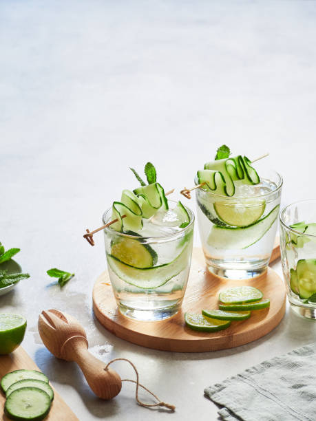 istock Glasses with fresh cucumber water garnished with thin, wavy cucumber strips on a skewer. Round wooden board and lime slices. 1462200138