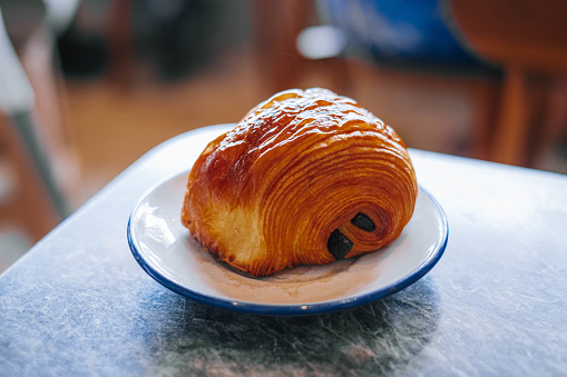 A chocolate croissant or pain au chocolat in a white small plate in a marble table with bokeh. Isolated.