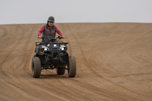 Latin adult man driving a quad bike in a sandy terrain in a desert