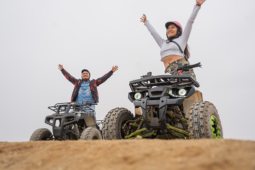 Two happy friends raising the arms on quad bikes on a beach