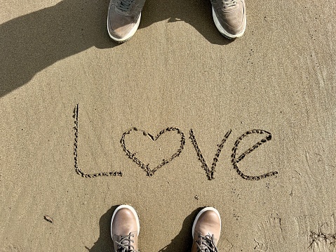 love, hand written love word on sand. female and male feet standing on a sandy beach. romance on beach with copy space. romantic relationship concept