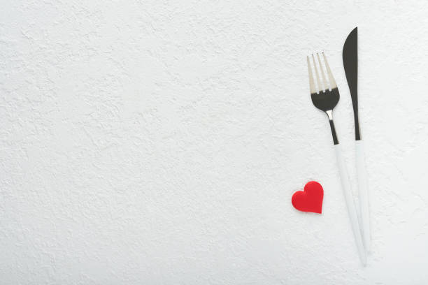 Valentines day romantic table setting. Empty or closeup of a dinner black plate, knife, fork and decorative silk hearts on white background. Holiday concept. Copy space for inscriptions.