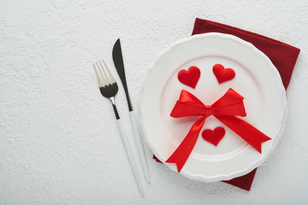 istock Valentines day romantic table setting. Empty or closeup of a dinner black plate, knife, fork and decorative silk hearts on white background. Holiday concept. Copy space for inscriptions. 1462205108