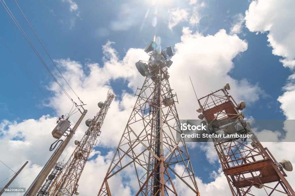 Cell and radio antennas next to the dirt road in the countryside. Communications Tower Stock Photo