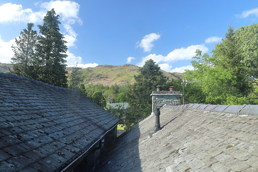 Elterwater, English Lake District, Cumbria, England, UK - Looking across slate tiles and chimneys of holiday cottage roofs towards the hills of the English Lake District