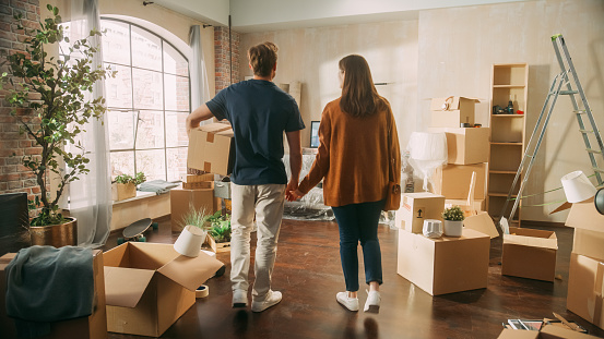 Family New Home Moving in: Happy and Excited Young Couple Enter Newly Purchased Apartment. Beautiful Family Happily Holding Hands. Modern Home Ready for Decorations