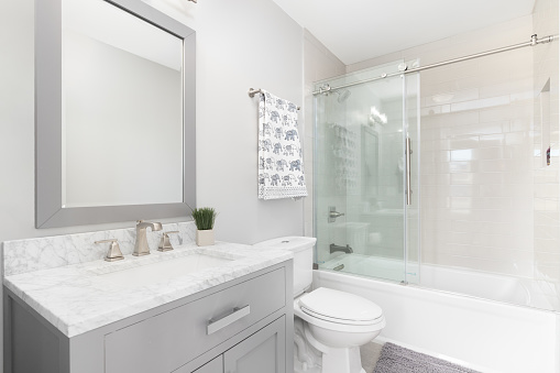 A beautiful bathroom with a grey cabinet, white marble countertop, and a tiled shower with a sliding glass door.