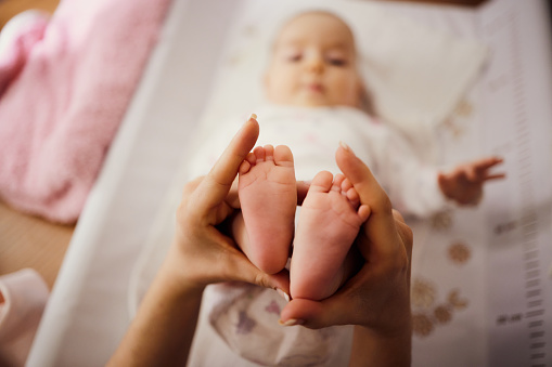 Close up of unrecognizable single mother holding her baby's feet in hands. Part of chronological photo series of growing up.