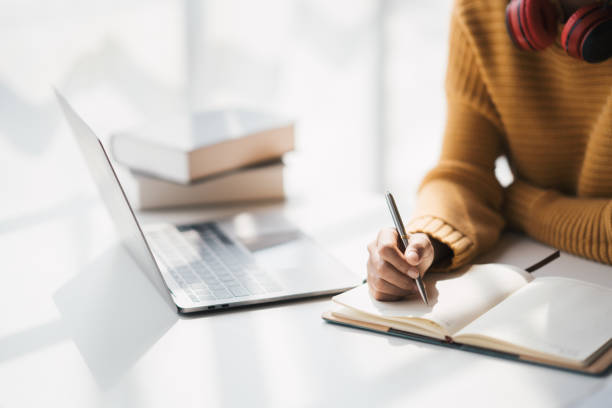 istock Young adorable Asian woman writhng on notebook while doing on her homework for the class. Doing homework at home comfortable. 1462214313