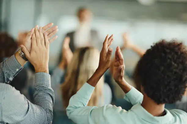 Back view of entrepreneurs congratulating their colleague on successful education event in board room. Focus is on black woman's hands.