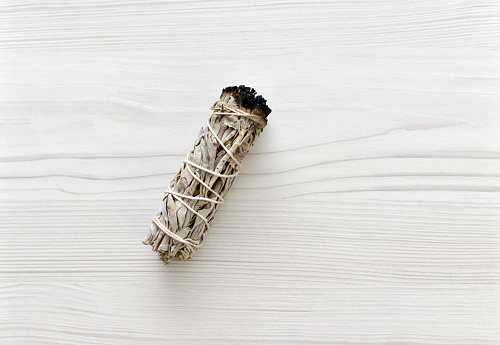 Closeup of a white sage smudging bundle on a whitewashed wood background.