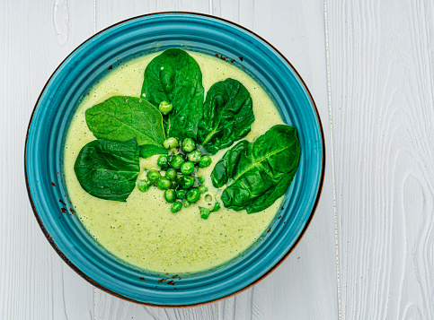 Spinach cream soup in bowl on white rustic table. Healthy and delicious food. Photo for the menu.