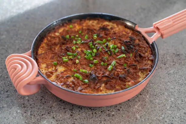 Pink cast iron skillet casserole dish with cheese and green onions. Wide shot.