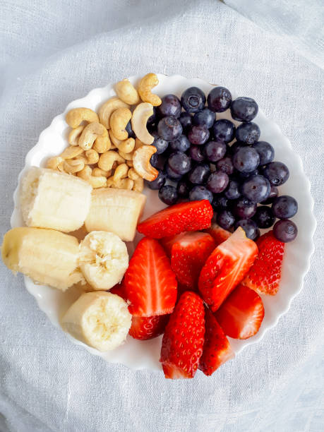 Healthy snack. Cashew nuts, banana, blueberries and strawberries on white plate.