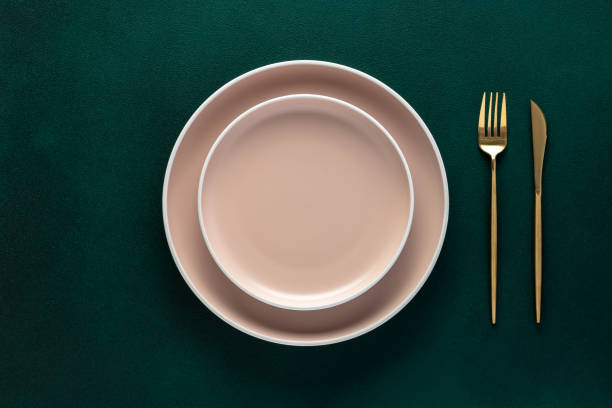 istock Empty beige plate, golden fork and knife on a dark green background. Top view, copy space. Table setting. Flat design. 1462228178