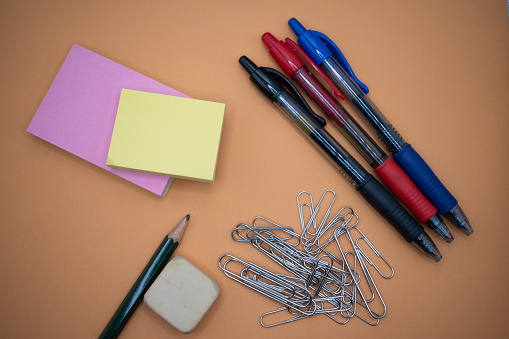 Pen, pencils, paper clips and post-its on an orange background