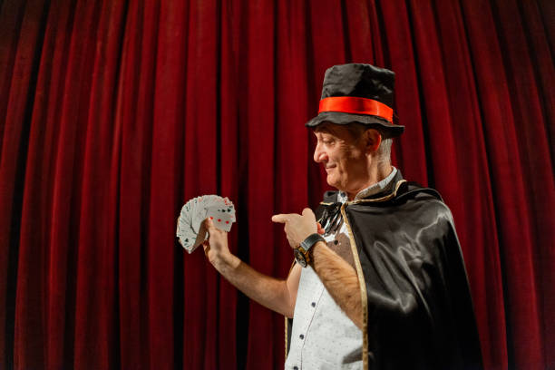 Portrait of the senior male magician, wearing a tail coat and cylinder while performing magic tricks on the stage at the theatre