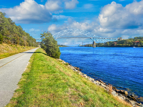 A two lane bicycle trail runs adjacent to the Cape Cod Canal on both sides of the waterway and is popular for walkers, bikers, rollerblades and the like. .  This view is of the mainland side looking toward the Sagamore Bridge (1935) on a bright October afternoon.