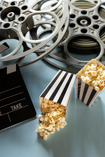 This is a conceptual photo relating to going out to the movies or watching a movie at home. There are two old retro movie reels on a light blue background with two bags of popcorn.