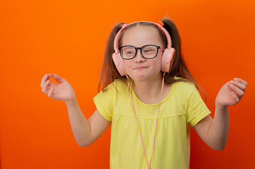 Girl with Down syndrome listens to music. Orange background