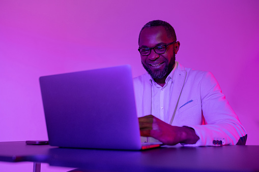 A black programmer works using a laptop computer. the man works at night. office with neon lighting
