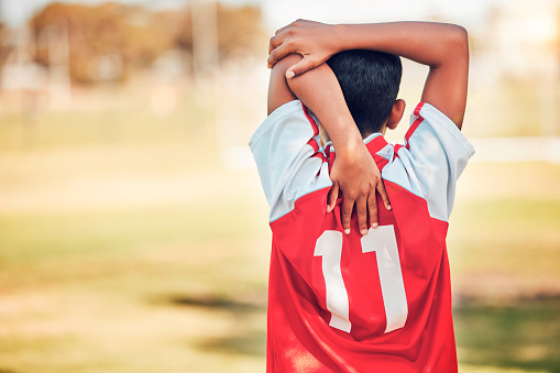 Soccer, football and boy stretching arm getting ready for training, game or competition. Sports, back view or soccer player warm up on grass field preparing for practice, exercise or workout outdoors