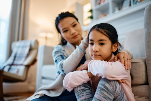 Come on dear, tell your mom whats bothering you! Sad Asian girl being consoled by her mother at home. asian parent and child sad stock pictures, royalty-free photos & images