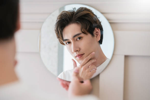 istock Closeup portrait of handsome beautiful asian boy with mirror makeup routine with copy space. Beauty influencer guy with perfect glow hand touch skin dress up. Healthcare man lifestyle cosmetic blogger 1462290001