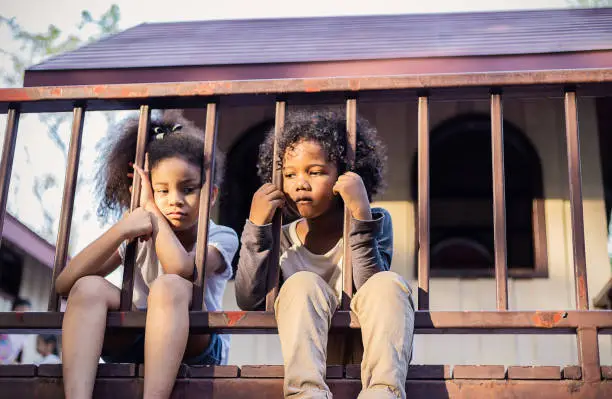 Multicultural little children sitting behind the fence. Homeless orphan stressful kids, education human right day concept. Young homeless boys girls emotional on the bridge, poverty city street