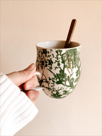 A Woman's Hand Wearing a Cream-Colored Cozy Sweater Holding a Green & Cream Mug With Hot & Healthy Mushroom Coffee in the Winter of 2023