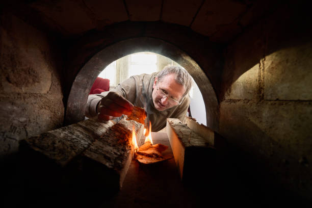 Middle aged man makes  fire in wood burning stone oven.