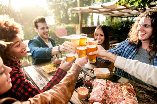 Young multiracial people drinking beer at brewery bar out doors - Happy family having barbecue party in backyard restaurant patio - Concept about friends enjoying time  together - Focus on pint glass Young multiracial people drinking beer at brewery bar out doors - Happy family having barbecue party in backyard restaurant patio - Concept about friends enjoying time  together - Focus on pint glass big family sunset stock pictures, royalty-free photos & images