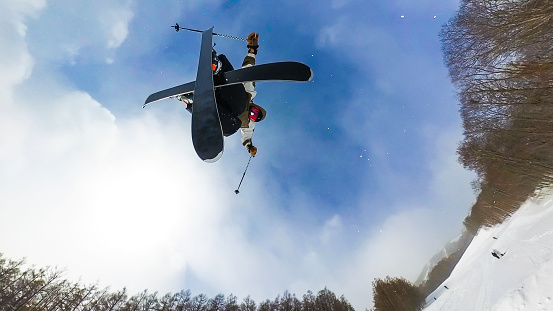 A wide angle directly below view of a freestyle skier doing a jump on a sunny day.