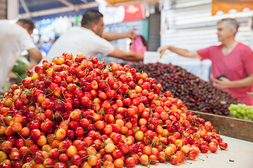 Tel Aviv, Israel - June 17, 2022:  A heap of fresh, bright red and yellow Rainier cherries on display at Carmel Market, Shuk Hacarmel, in Tel Aviv.  In the background, a shopper is buying cherries from the farmer.